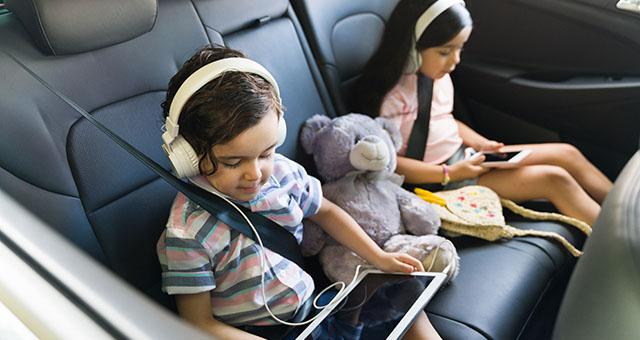 Two children riding in a car using tablets and headphones