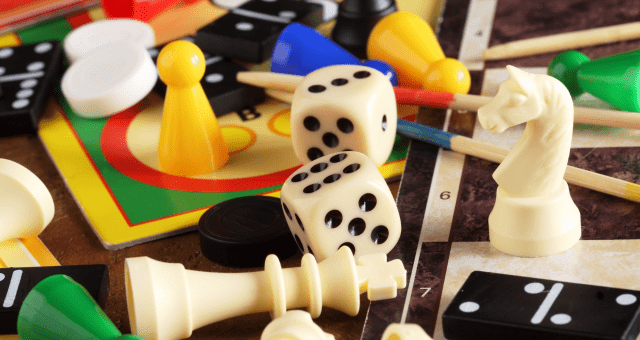 A close-up of various classic board game pieces including dominoes, dice, playing cards, and chess pieces.
